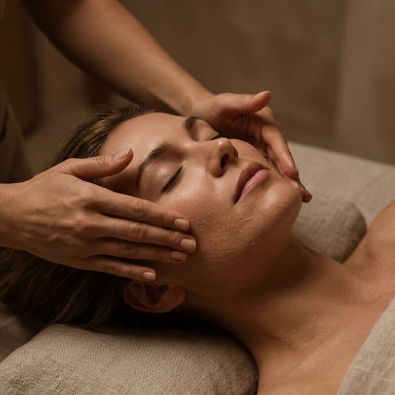 Hands working across the brow of a woman lying with her eyes closed.