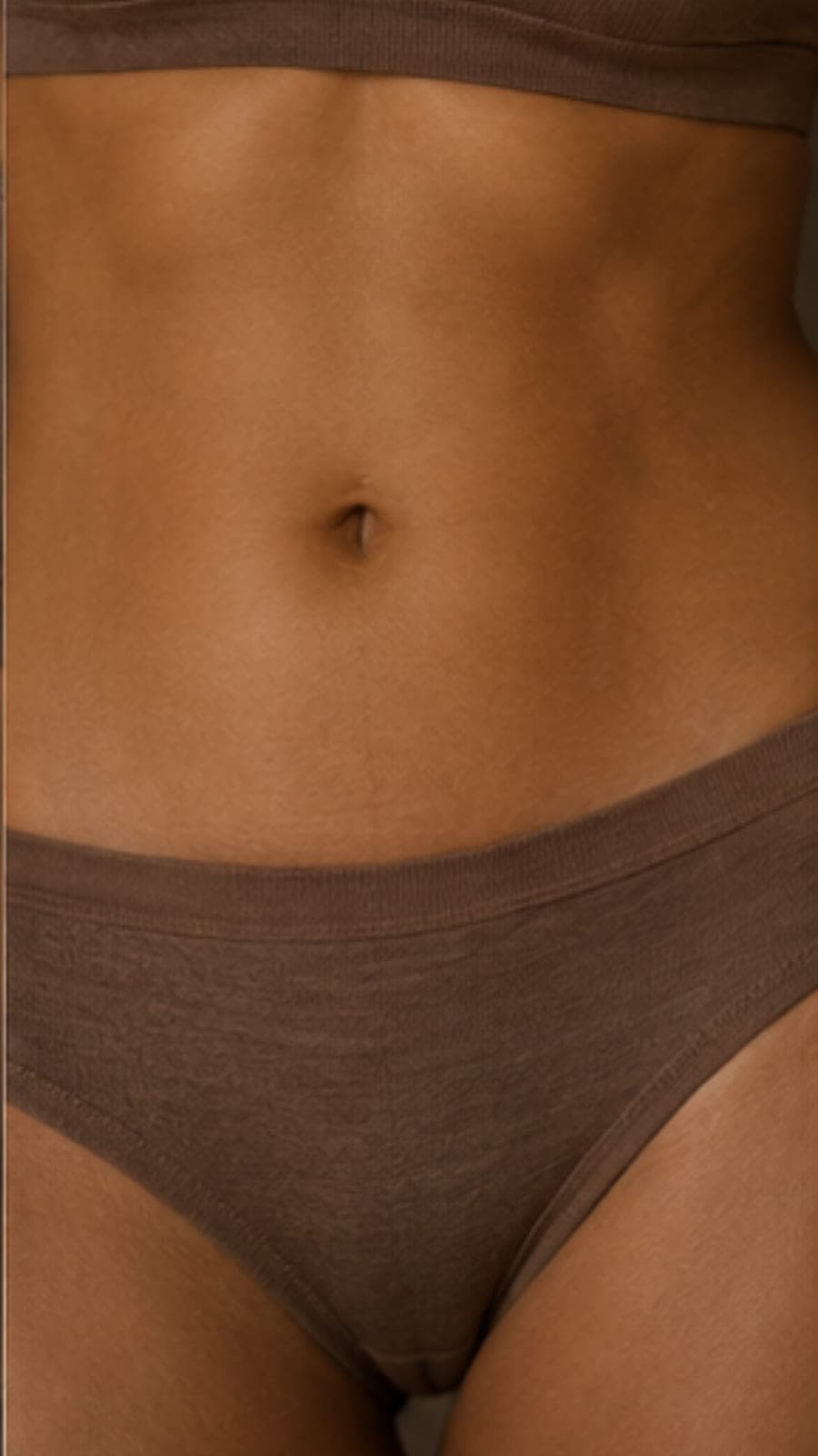 A close view of a torso in soft brown underwear against a plain wall.